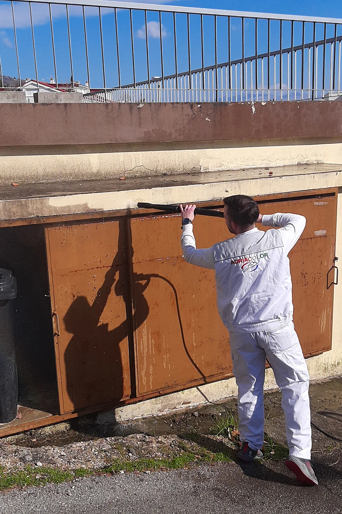 Radnik u radnoj odjeći Adriacolor pere metalna vrata visokotlačnom pumpom.